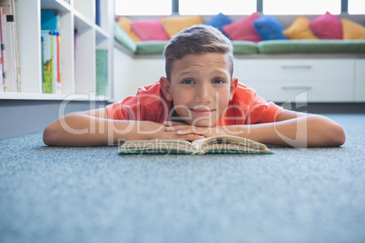 Schoolboy lying on floor and reading a book in library