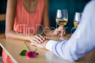 Mid section of couple holding hands while having glass of wine
