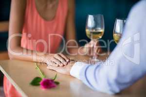 Mid section of couple holding hands while having glass of wine