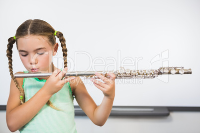 Schoolgirl playing flute in classroom