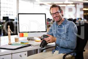 Creative businessman holding camera by computer desk