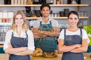 Smiling waiter and two waitresses standing with arms crossed