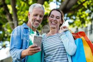 Mature couple using mobile phone by tree