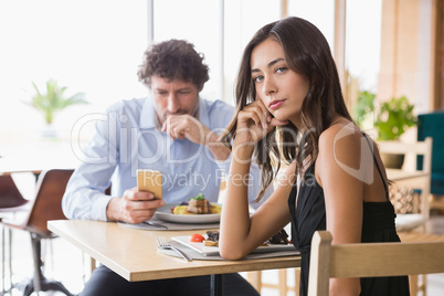 Portrait of woman sitting while man using mobile phone in backgr