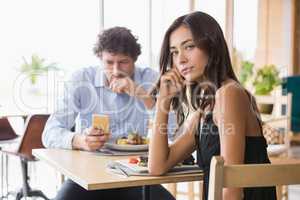 Portrait of woman sitting while man using mobile phone in backgr
