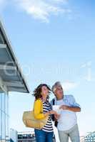 Smiling couple holding map against sky