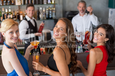 Happy female friends holding glass of cocktail at bar counter