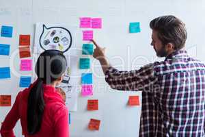 Colleagues discussing about sticky notes in office