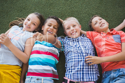 Smiling schoolkids lying on grass in campus