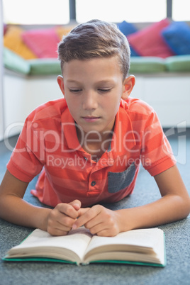 Schoolboy lying on floor and reading a book in library