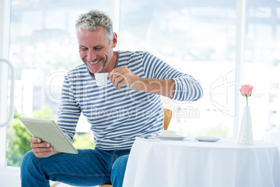 Smiling mature man holding digital tablet while having coffee