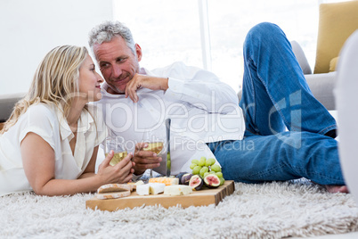 Romantic couple with white wine and food while lying on rug