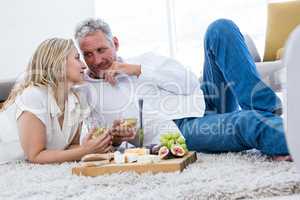 Romantic couple with white wine and food while lying on rug