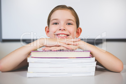 Portrait of smiling girl leaning on stack of books in class room