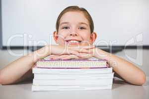 Portrait of smiling girl leaning on stack of books in class room