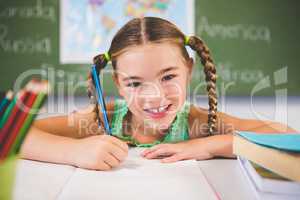 Portrait of smiling schoolgirl doing homework in classroom