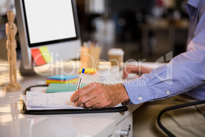 Businessman writing on paper at computer desk