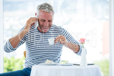 Smiling mature man talking on phone while having coffee