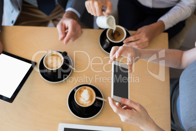 Colleagues having a cup of coffee while using mobile phone and d