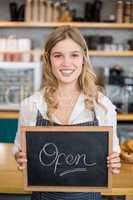 Smiling waitress showing chalkboard with open sign at cafe