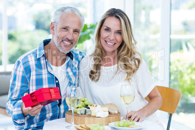 Mature man holding gift while sitting beside wife