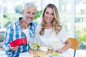 Mature man holding gift while sitting beside wife