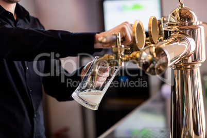 Bartender pouring beer from faucet in pint glass