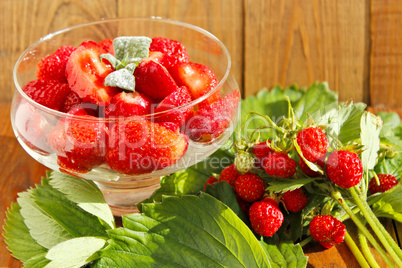 strawberries in transparent bowl and bunches with leaves