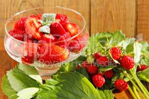 strawberries in transparent bowl and bunches with leaves