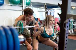 At gym. Sexy coach helps girl to do squat