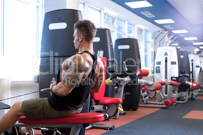 At gym. Tattooed bodybuilder trains on simulator