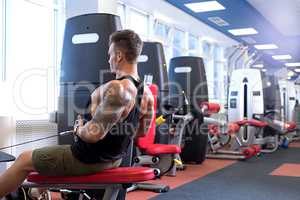 At gym. Tattooed bodybuilder trains on simulator