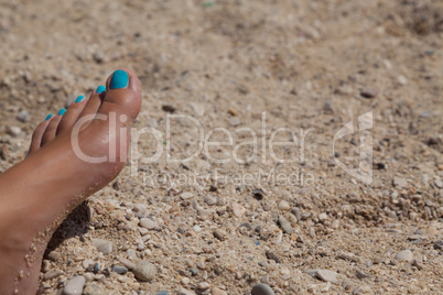 female foot with cyan pedicure in beach sand