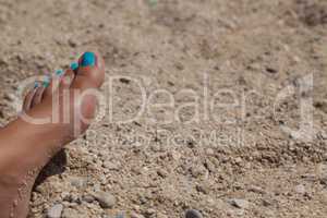 female foot with cyan pedicure in beach sand