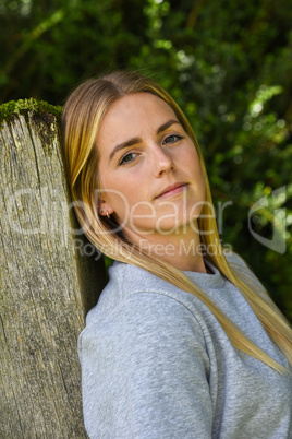 Close-up of blonde leaning against wooden gatepost