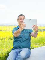Man with tablet PC on the canola field with wind turbine