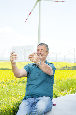 Man with tablet PC on the canola field with wind turbine