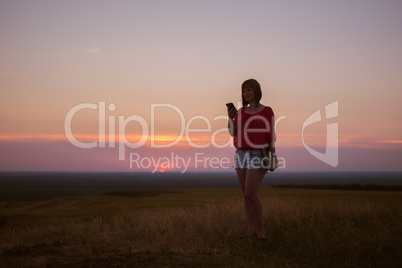 Young girl uses smartphone on sunset background