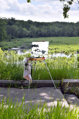 Hands of the artist with a brush, paint a picture on an easel in the open air