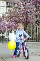 Child with bicycle and balloon in the city under blossoming cherry trees