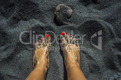 Female bare feet with red nails on black sand beach