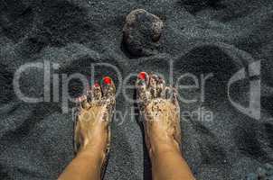 Female bare feet with red nails on black sand beach