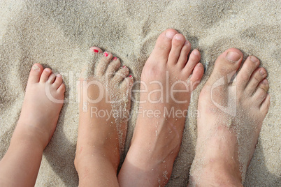 feet of father mother and their daughters on beach sand