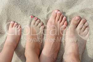 feet of father mother and their daughters on beach sand