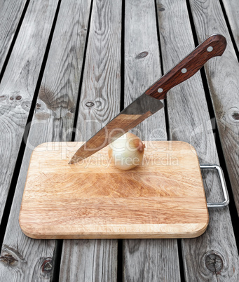 Knife,onion and a cutting board  on  wooden table