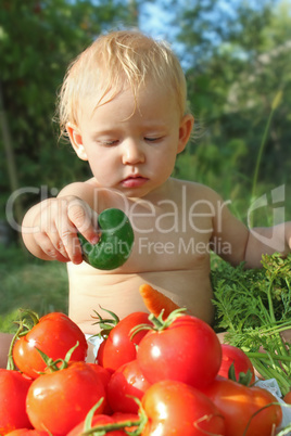 baby with cucumber on the heap of ripe tomatoes
