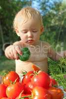 baby with cucumber on the heap of ripe tomatoes