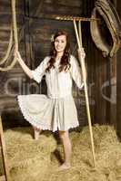 Young woman with wooden rake in the barn