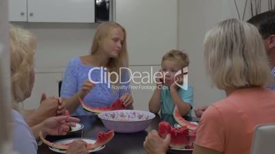 Family with child eating watermelon in the kitchen