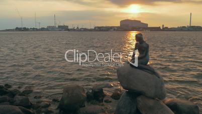 Mermaid statue on city waterside at sunset
